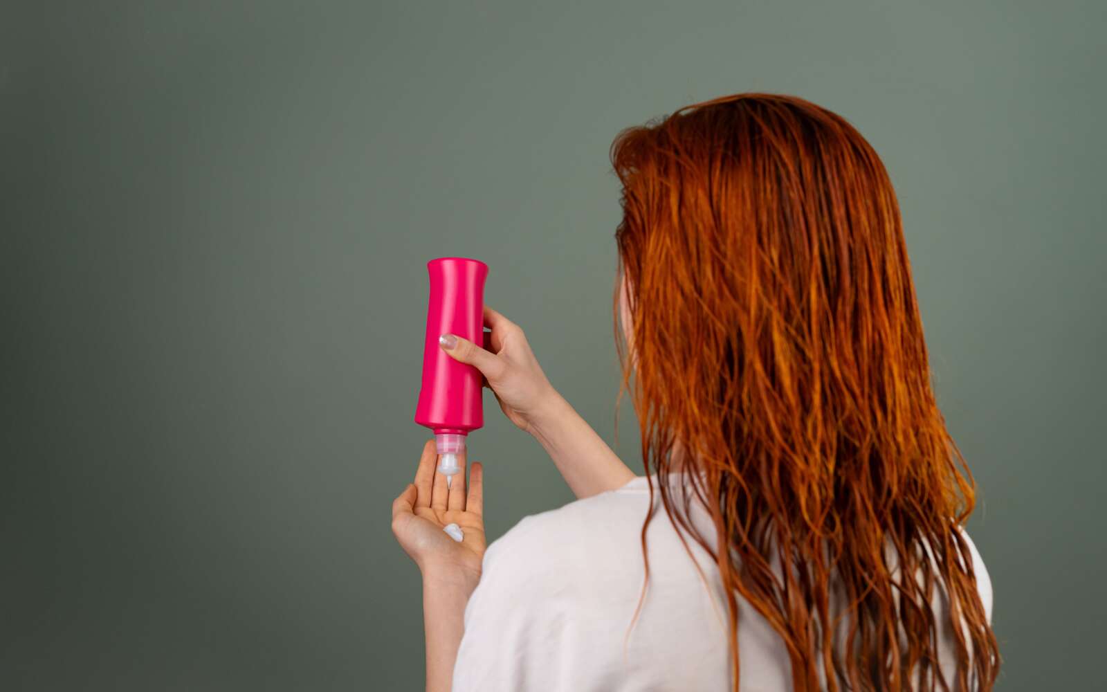 Mujer adulta con cabello rojo mojado aplicando acondicionador. Rutina de cuidado del cabello.