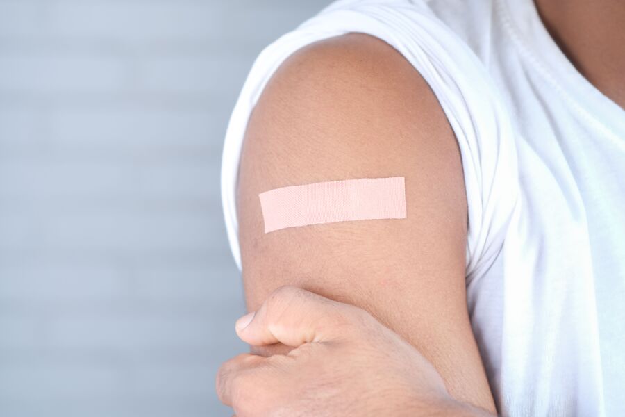 Una imagen en primer plano de un adulto con un vendaje en la parte superior del brazo, probablemente después de la vacunación.