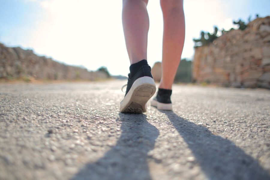 Una persona camina por un camino rural soleado con zapatillas de deporte, proyectando una larga sombra.