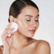 Cuidado de la piel y tratamiento saludable de la mujer que quita el maquillaje de la cara con un algodón, aislado en blanco
