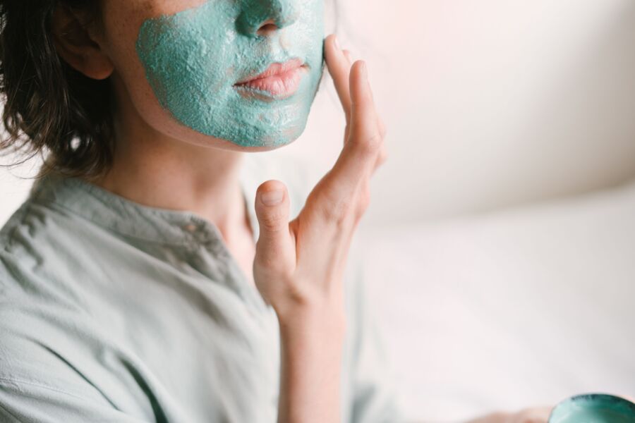 La mujer joven aplica una mascarilla facial rejuvenecedora en el interior para el cuidado de la piel y la relajación.