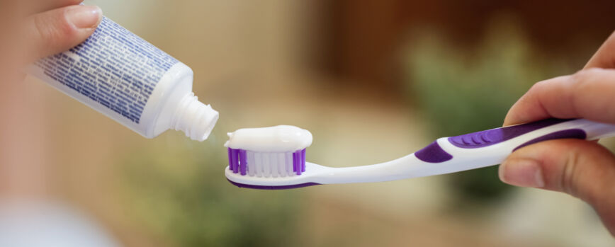 Primer plano de una mujer irreconocible aplicando pasta de dientes en un cepillo de dientes en el baño