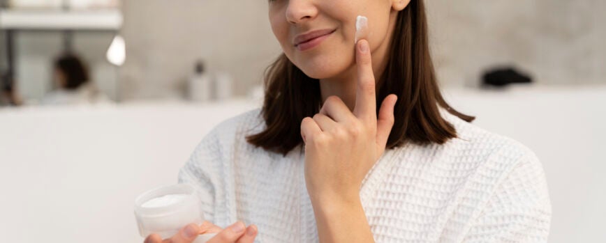 Mujer joven aplicar crema hidratante en el rostro antes de tomar un baño