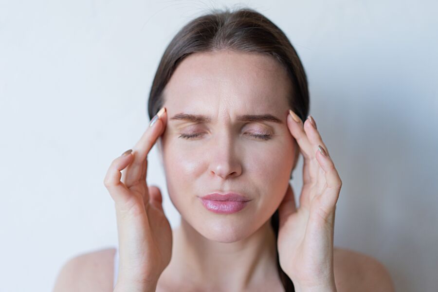 Primer plano de una mujer con los ojos cerrados sosteniendo sus sienes, mostrando signos de migraña o dolor de cabeza.
