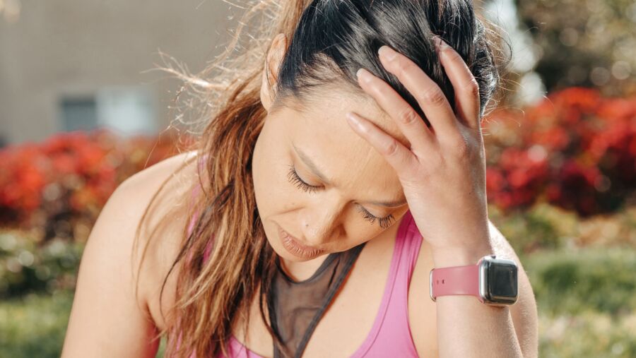 Primer plano de una mujer con dolor de cabeza sentada al aire libre con un reloj inteligente.