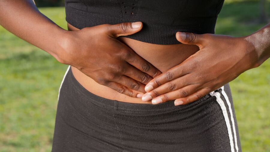 Primer plano de una persona sosteniendo su estómago, indicando dolor abdominal al aire libre.