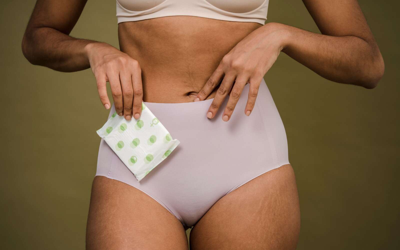 Recorte mujer anónima en sujetador y braga rosa con toalla sanitaria para periodo crítico sobre fondo de olivo