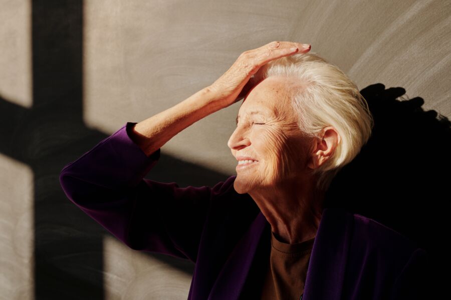 Una anciana sonriendo a la luz del sol, disfrutando de un momento sereno en el interior.