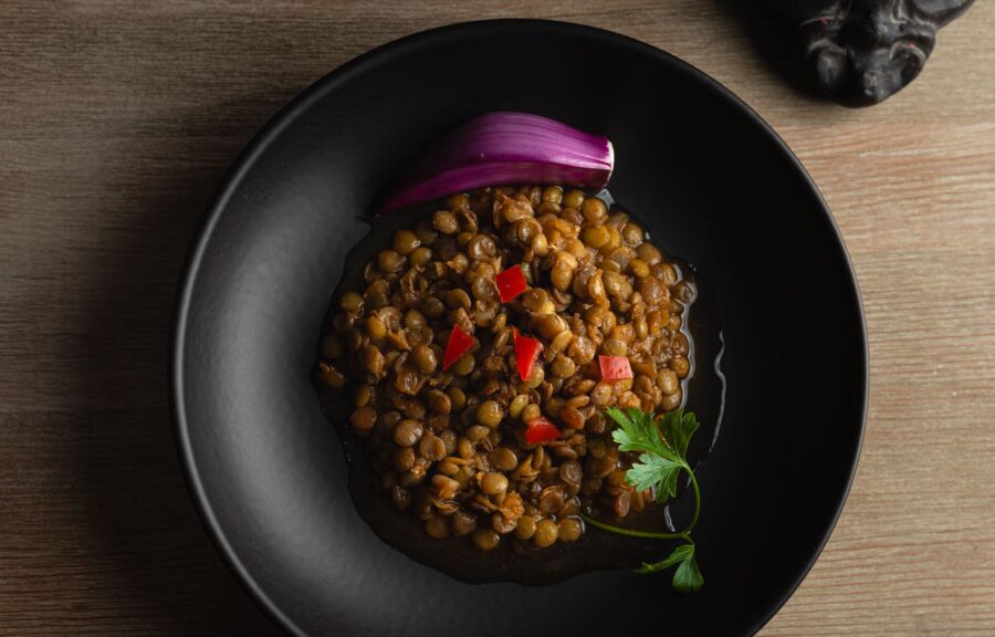 Vista superior de un salado plato de lentejas adornado con cebolla y perejil en un bol negro.