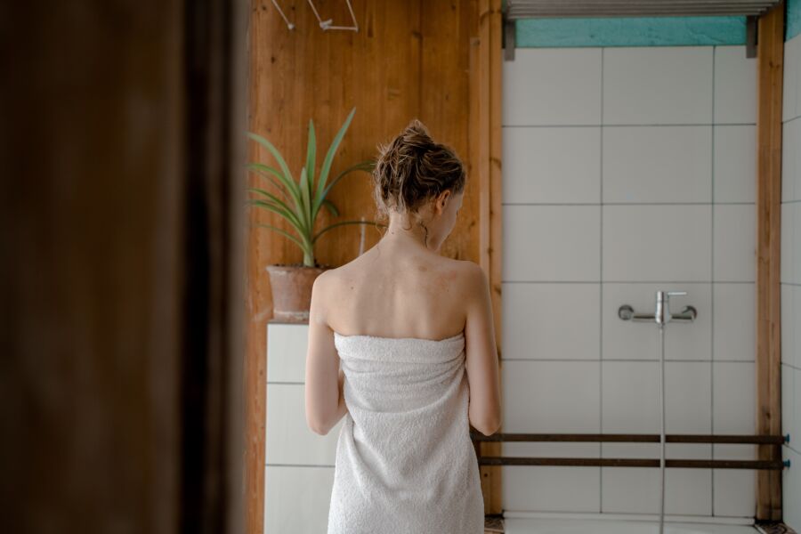 Vista trasera de una mujer envuelta en una toalla en un baño sencillo y moderno.
