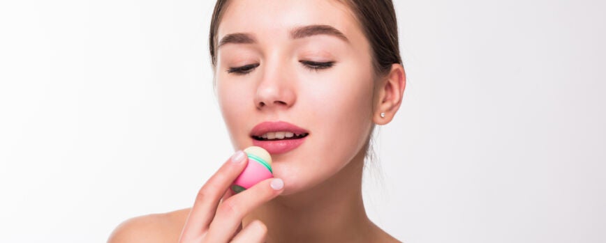 Mujer joven que aplica bálsamo labial higiénico en la pared blanca