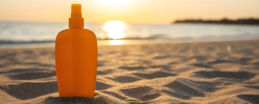Botella de protector solar en una playa de arena durante la puesta de sol