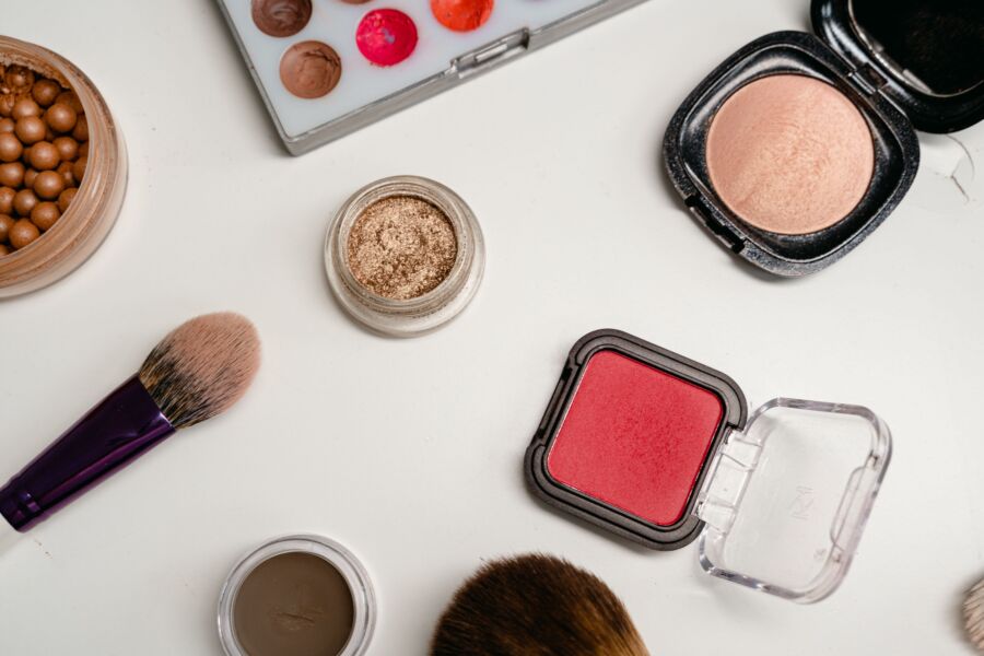 Colocación plana de varios productos de maquillaje, incluidos pinceles, polvos y cremas sobre una superficie blanca.
