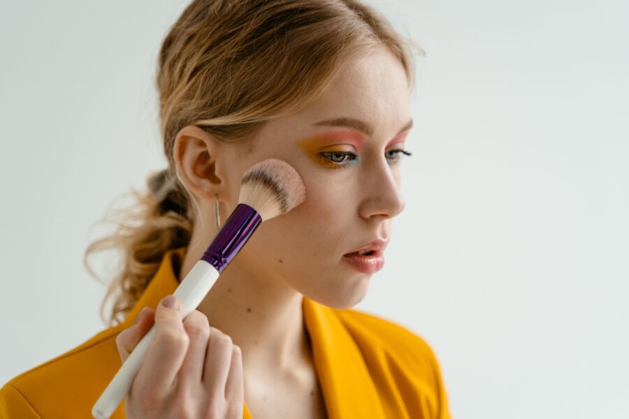 Mujer usando una brocha de maquillaje para aplicar rubor, mostrando belleza y cosméticos en interiores.