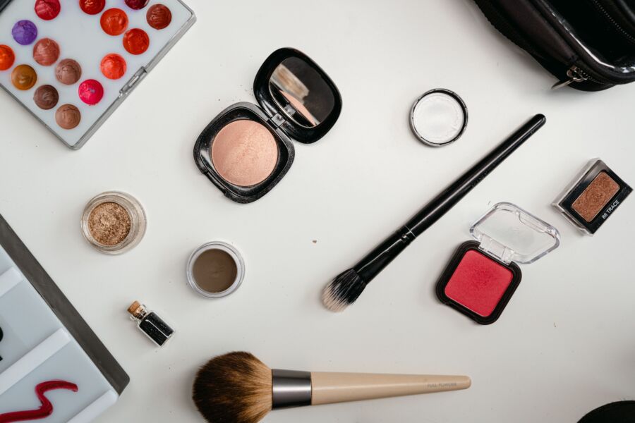 Una capa plana de productos de belleza que incluyen sombra de ojos, pinceles y rubor sobre una superficie blanca.