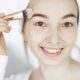 Retrato de una joven sonriente aplicando maquillaje con un pincel en interiores.