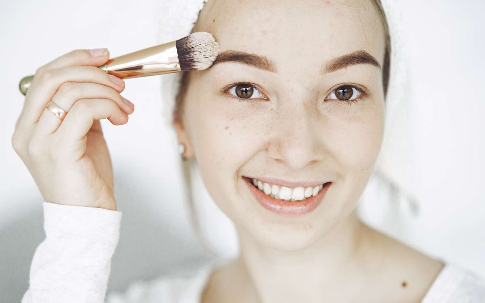 Retrato de una joven sonriente aplicando maquillaje con un pincel en interiores.