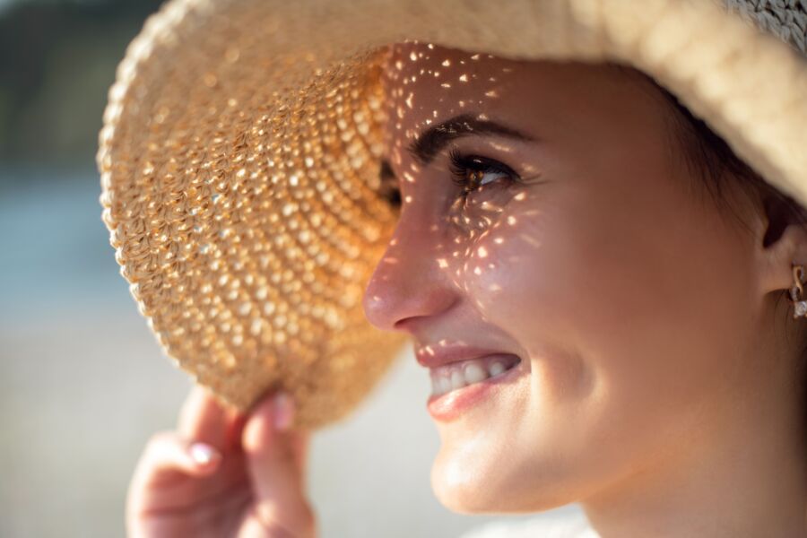 Retrato en primer plano de una mujer sonriente con un sombrero para el sol, abrazando la luz del sol al aire libre.