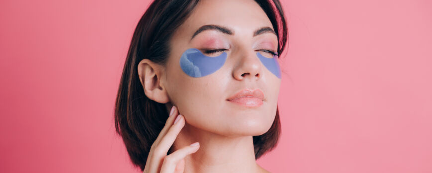 Retrato de primer plano de una joven y bella mujer en topless hombros abiertos con almohadillas de colágeno azul debajo de los ojos. Concepto de belleza.