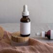 Configuración minimalista de botellas para el cuidado de la piel con tapas de bambú sobre una superficie textil.