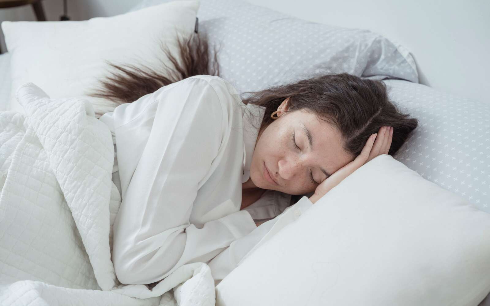 Una mujer serena descansa cómodamente en la cama con almohadas y mantas suaves, abrazando la relajación.