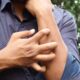 Un hombre con una camisa azul rascándose el brazo al aire libre, destacando la irritación de la piel.