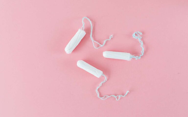 Imagen minimalista de tres tampones blancos sobre fondo rosa, ideal para temas de salud.
