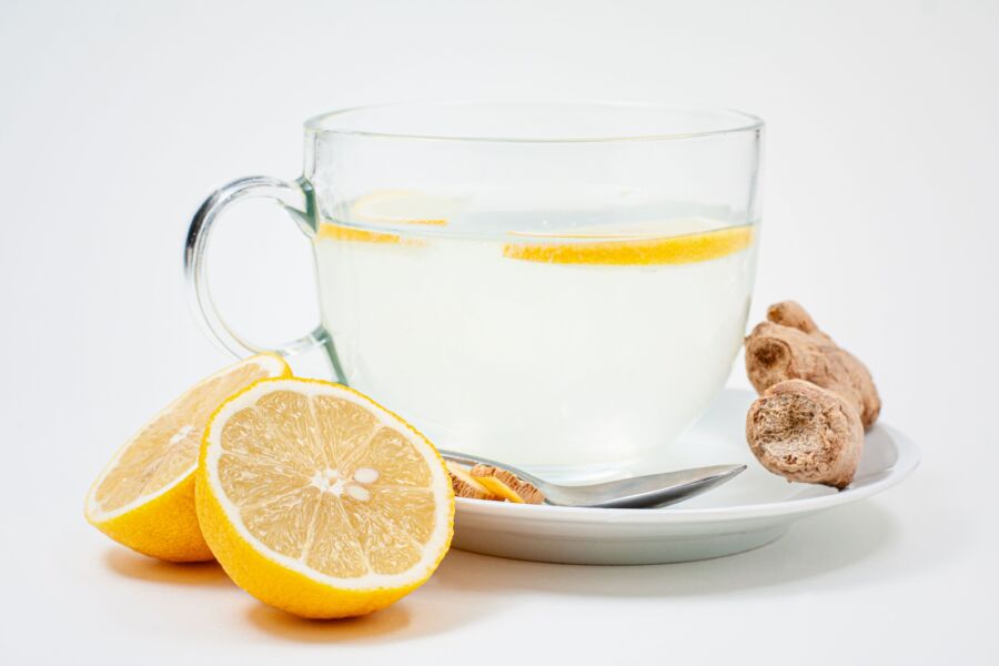 Una taza relajante de té de limón y jengibre con rodajas de limón fresco y raíz de jengibre sobre un fondo blanco.