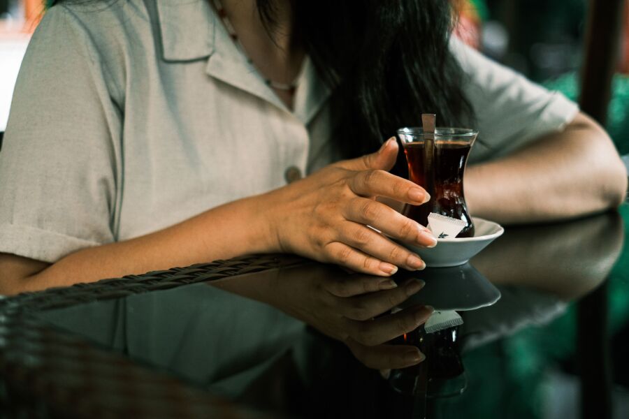 Primer plano de una mujer disfrutando del té en una mesa de café reflectante, creando un momento sereno.
