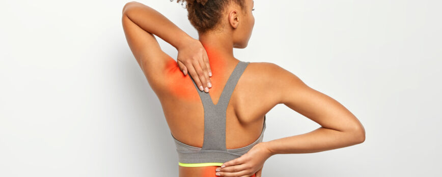 La mujer rizada sin rostro sufre de dolor de columna, usa sujetador deportivo, muestra la ubicación de la inflamación, aislada sobre fondo blanco.