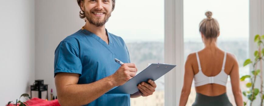 Terapeuta osteopático masculino sonriente con portapapeles y paciente en la clínica
