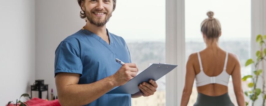 Terapeuta osteopático masculino sonriente con portapapeles y paciente en la clínica