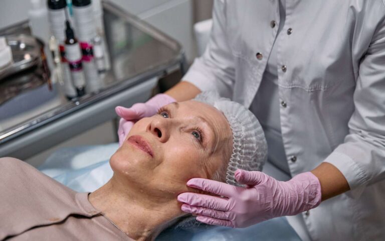 A mature woman in a spa receiving a relaxing facial treatment from a professional in a medical clinic setting.