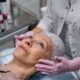 A mature woman in a spa receiving a relaxing facial treatment from a professional in a medical clinic setting.