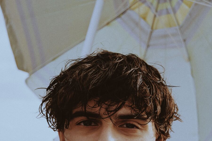 Retrato de media cara de un joven con el pelo desordenado bajo una sombrilla de playa.