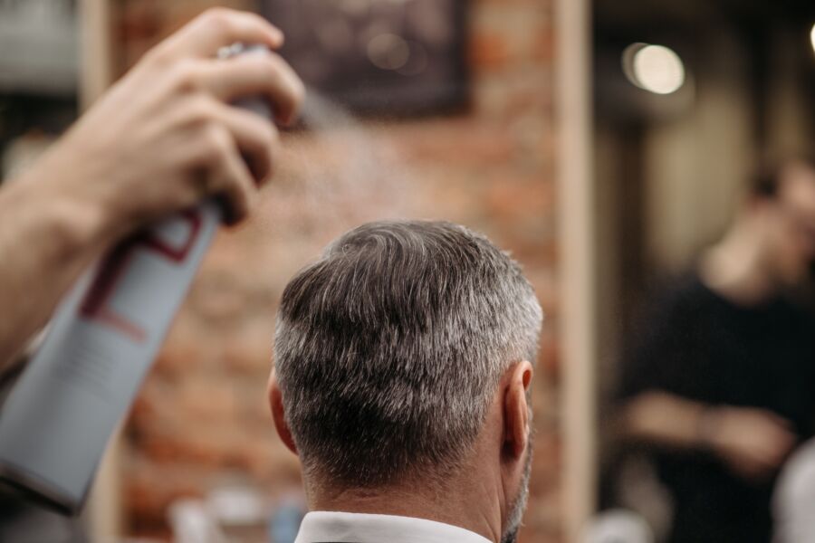 Un barbero profesional peina el cabello de un hombre con laca en una barbería urbana.