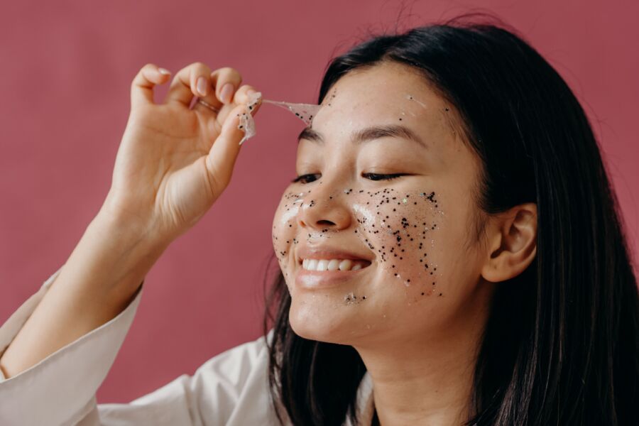 Primer plano de una mujer asiática sonriente que se quita una mascarilla brillante, destacando su rutina de cuidado de la piel.