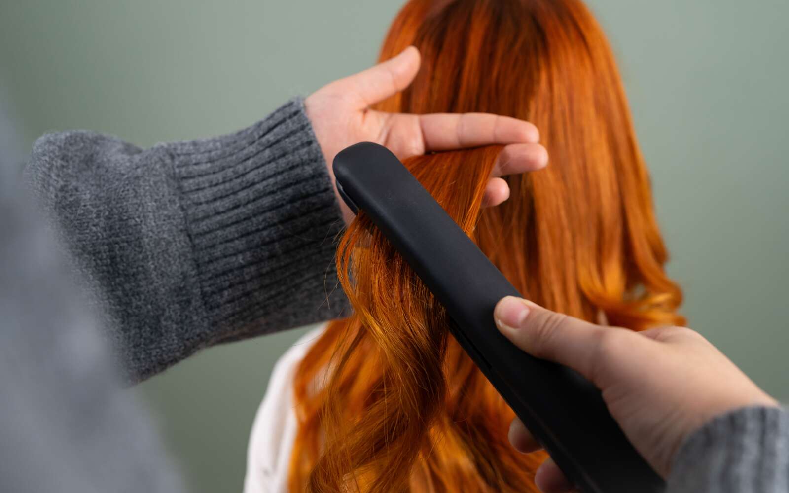 Manos peinando el pelo largo de color rojo con una plancha plana en interiores. Concepto de belleza y cuidado del cabello.