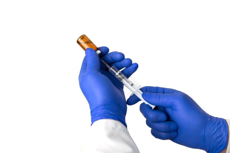 Médico irreconocible en guantes protectores azules con frasco de jeringa de llenado de fármaco con vacuna contra fondo blanco durante la pandemia de coronavirus