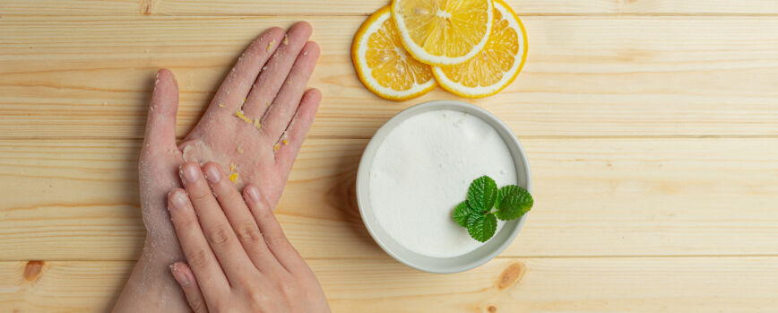Mujer joven aplicando exfoliante de limón natural en las manos contra la mesa de madera