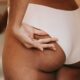 Vista posterior de una mujer étnica anónima en bikini con las manos en las nalgas contra el espejo en casa