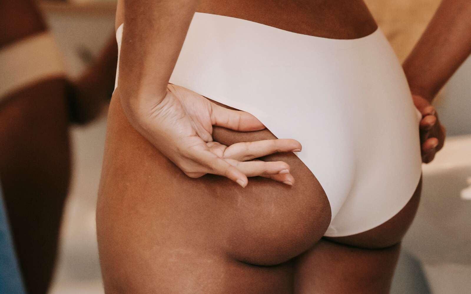 Vista posterior de una mujer étnica anónima en bikini con las manos en las nalgas contra el espejo en casa